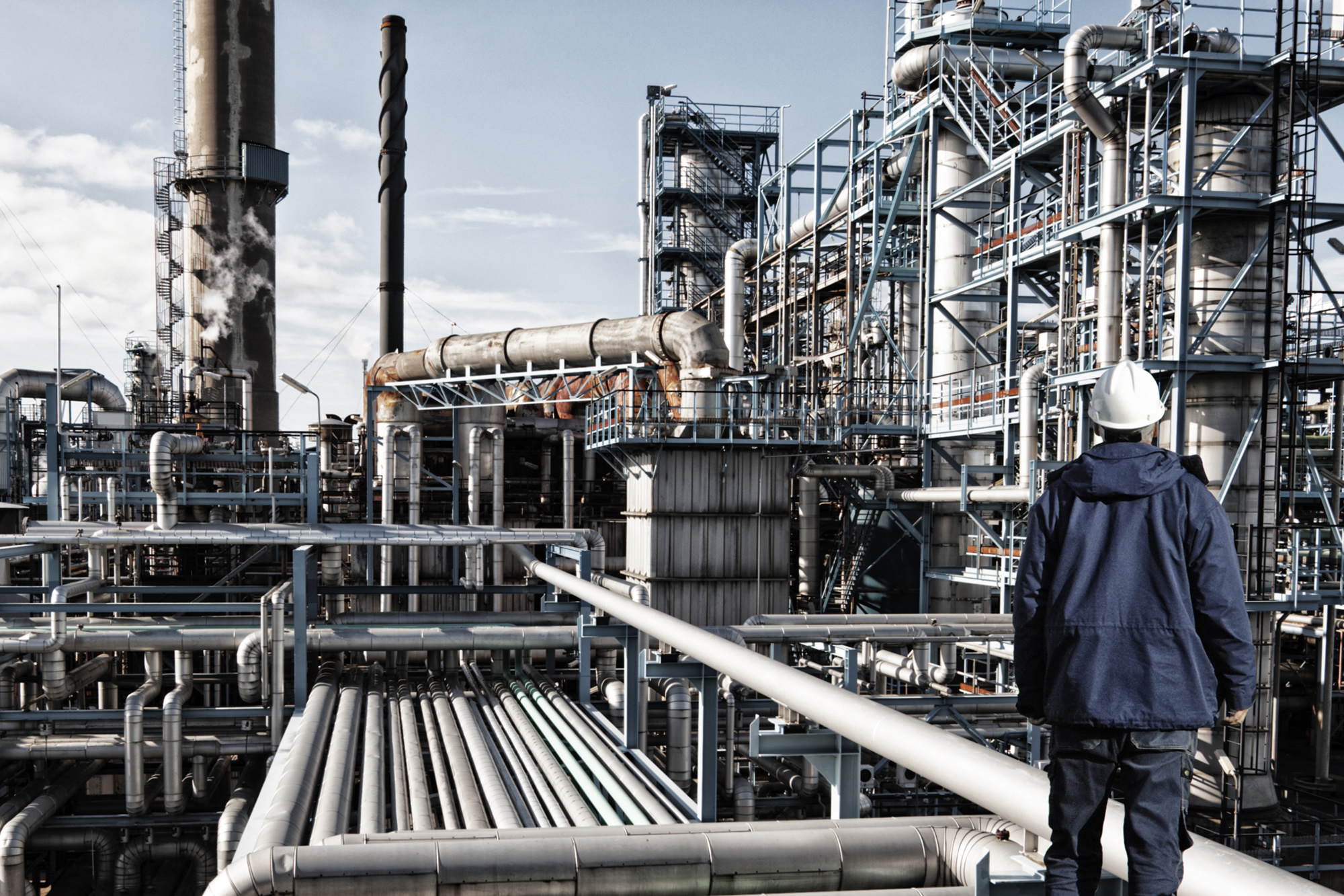 Image of an oil and gas worker standing in front of large refinery installation